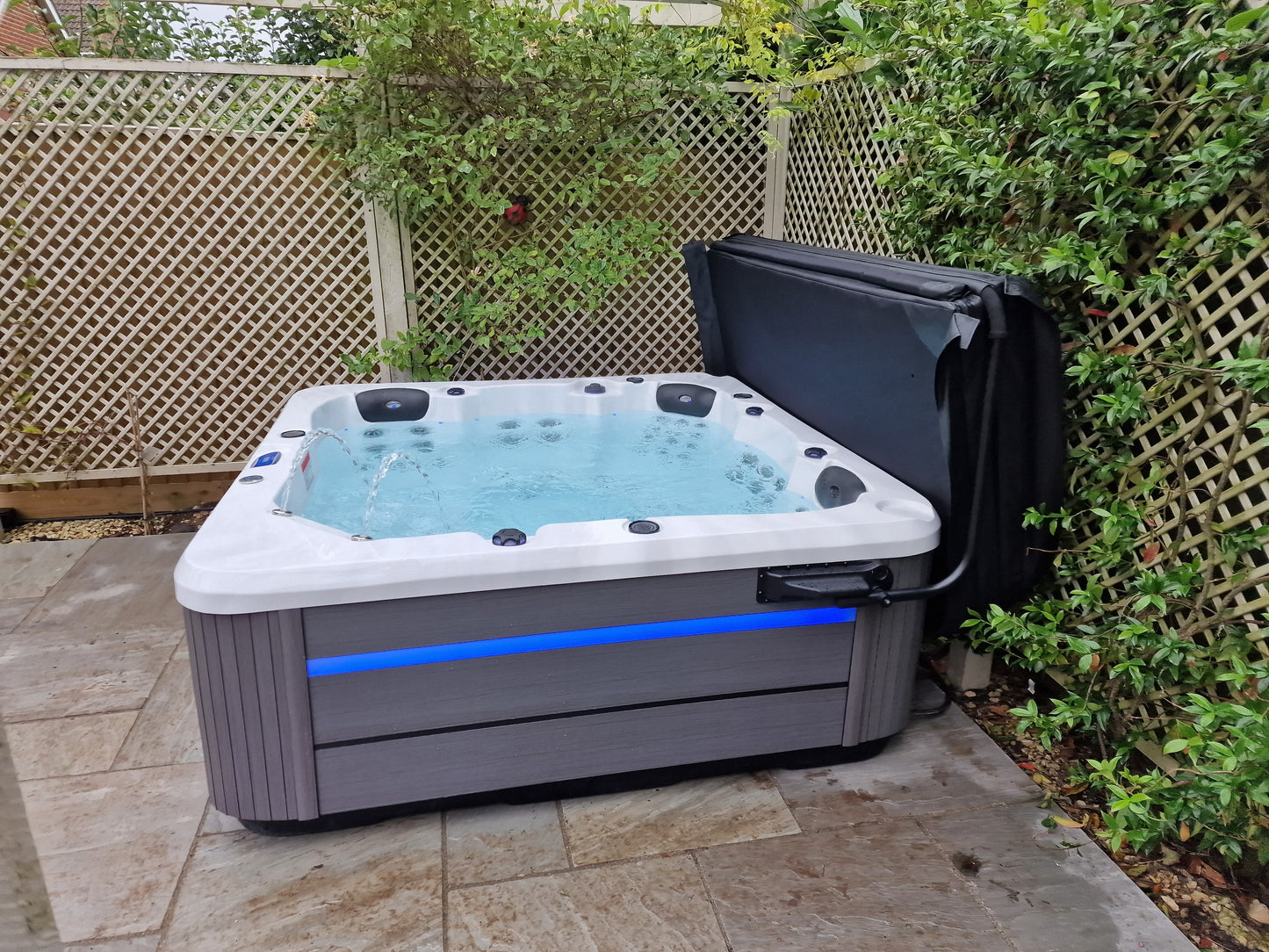 Hot tub with blue light on a patio area surrounded by greenery
