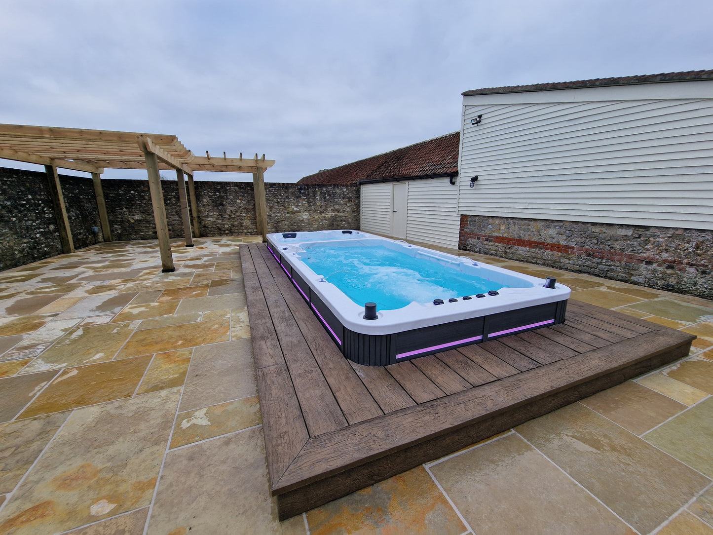 Inground dual temperature swimspa on a wooden platform with stone patio and building in the background