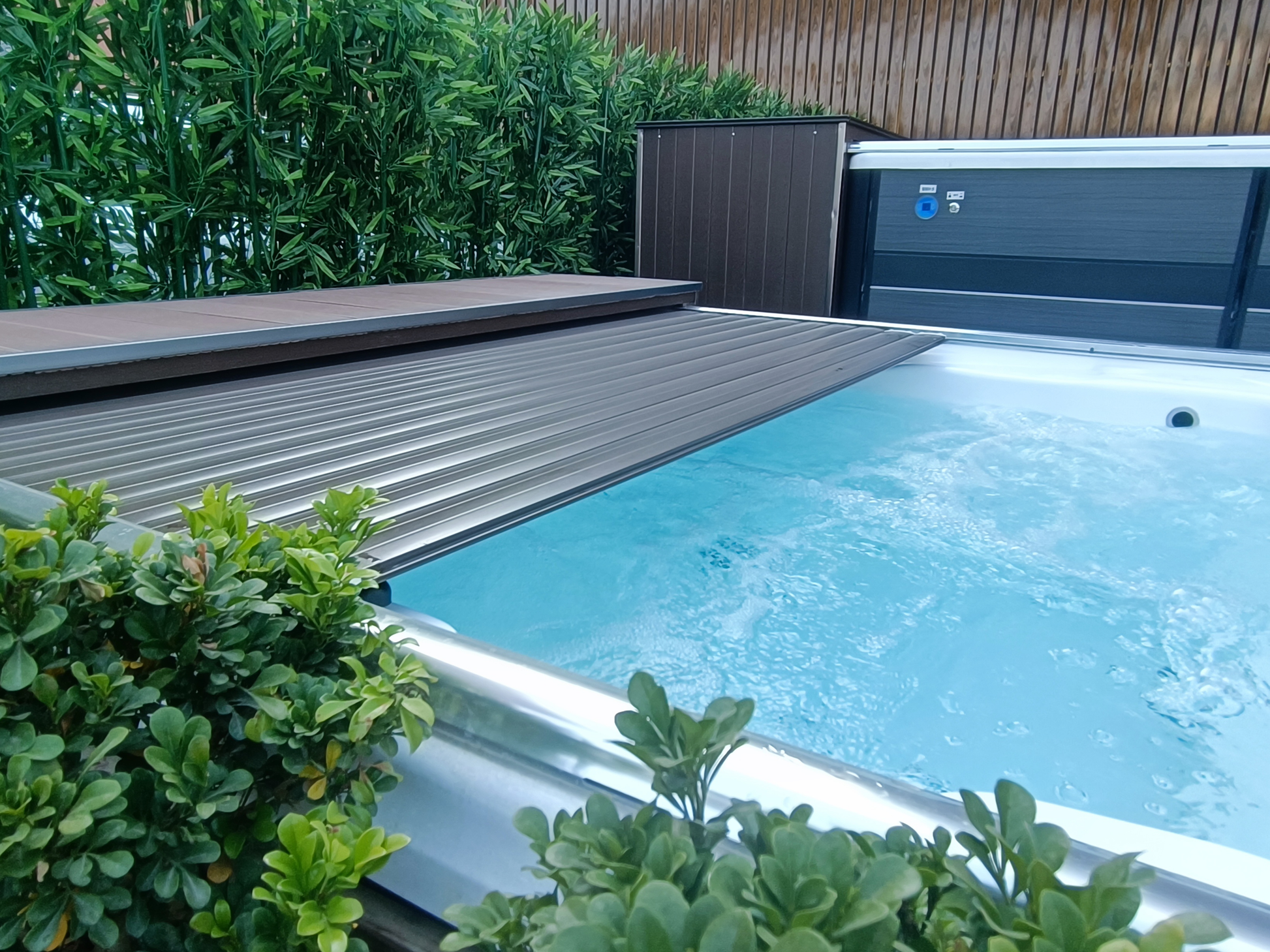 swim spa automated cover partially open with water visible, surrounded by greenery