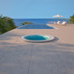 mosaic hot tub installed inground in a patio with a view of the ocean and clear blue sky.
